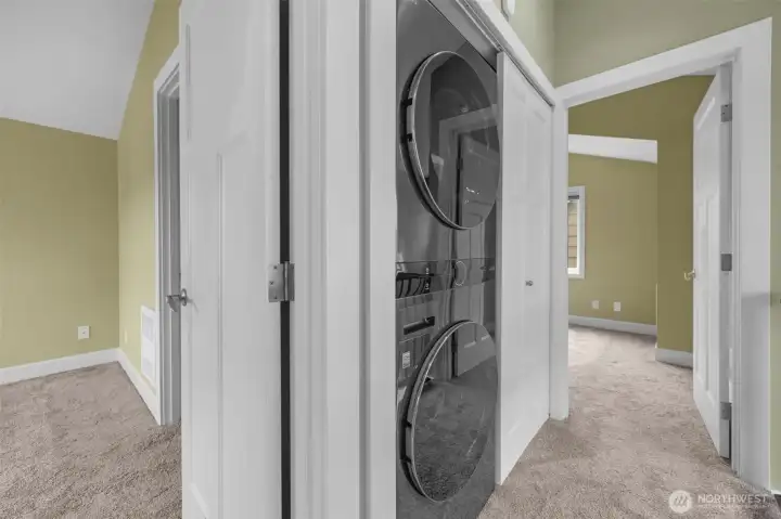 The top-floor hallway offers a clean, modern design featuring a convenient stacked washer and dryer for everyday ease. Sleek metal railings add a contemporary touch while enhancing the open feel and flow of the upper level.