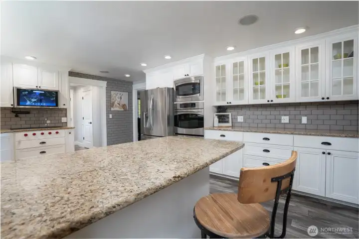 Granite counter tops and custom tile backsplash envelope the kitchens surroundings with Stainless steel appliances to include a double oven, microwave, dishwasher & French door fridge. The glass front upper cabinets allows you to display your favorite items. Door beyond leads to back entry, laundry room, 1/2 bath and garage
