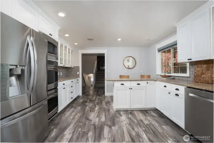 Another view if the kitchen looking towards the lower level and upper level - through the doorway to the right is the front entry. The flowing LVP is throughout the entire home is the perfect flooring for this lifestyle property.