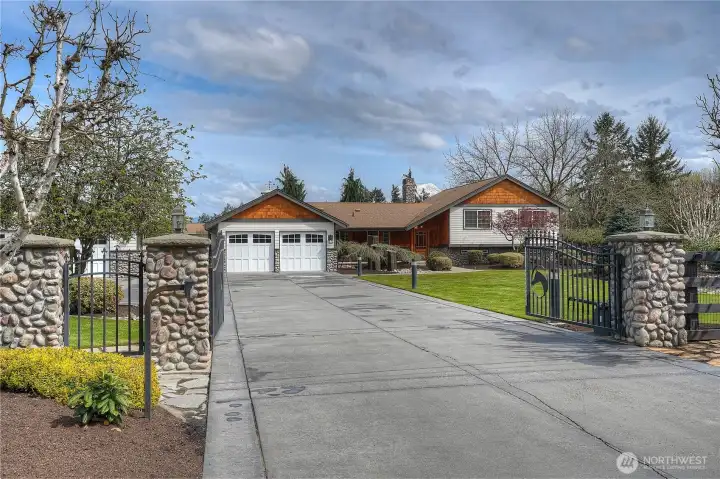 Enter through custom wrought iron gates with stone columns and onto impeccably maintained grounds framed by mature landscaping and wide-open pastures.