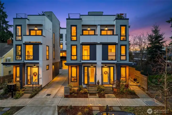 Modern multi-level townhome exterior featuring clean architectural lines and large windows with evening lighting.