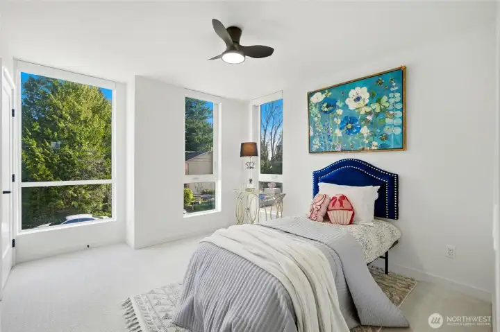 Additional bedroom featuring oversized windows, clean modern design, ceiling fan and ample natural light.