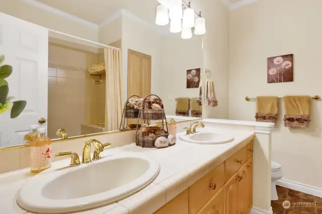 Twin sinks with tiled surfaces and a large tub & shower are featured in the bathroom