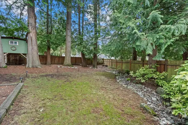Winter view of the fenced backyard featuring a grassy area for relaxation, a side garden, and a playhouse.