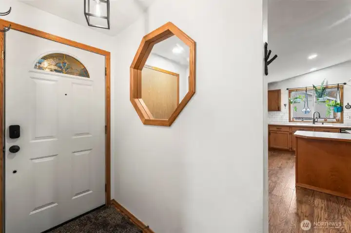 The entry includes a feature wall with a charming window that helps the entry feel bright and open. The kitchen can be seen behind the wall, and the door to the garage is visible through the window.
