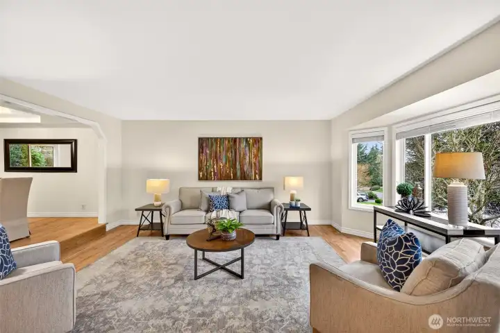 The living room is filled with natural light from a wide bay window, creating a bright and comfortable space for everyday living or entertaining. Refinished hardwood floors add warmth and continuity to this inviting main gathering area.