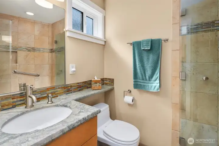 The guest en-suite bath: a glass shower and a band of iridescent mosaic tile that catches the light.