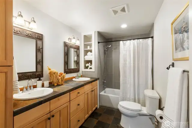 Beautifully refreshed bathroom with double sink vanity, tile shower, slate floors, and fun, whimsical fixtures.