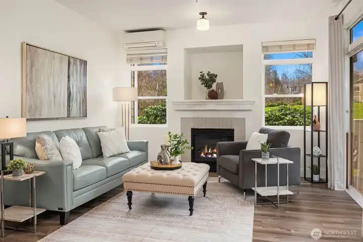 This beautifully styled living room is bathed in natural light from large windows framing lush green views, featuring a cozy fireplace, elegant furnishings, and an open layout that perfectly captures the warmth and comfort this home has to offer.