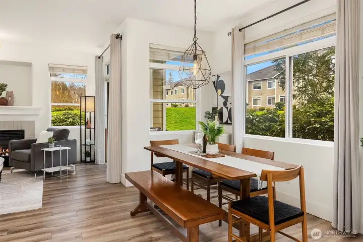 The dining area is a bright and inviting space, featuring large windows that flood the room with natural light and frame beautiful green views, a perfect setting for both casual meals and gathering with friends.