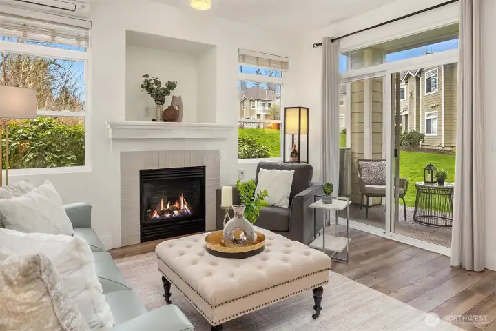 This cozy sitting area showcases the home's abundant natural light, elegant fireplace, and seamless access to the private patio beyond, a serene and inviting space perfectly framed by lush green views.