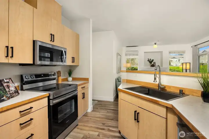 This angle of the kitchen showcases the full suite of appliances, undermount sink, and bright window, a well-equipped and efficiently designed space that makes meal preparation a pleasure.