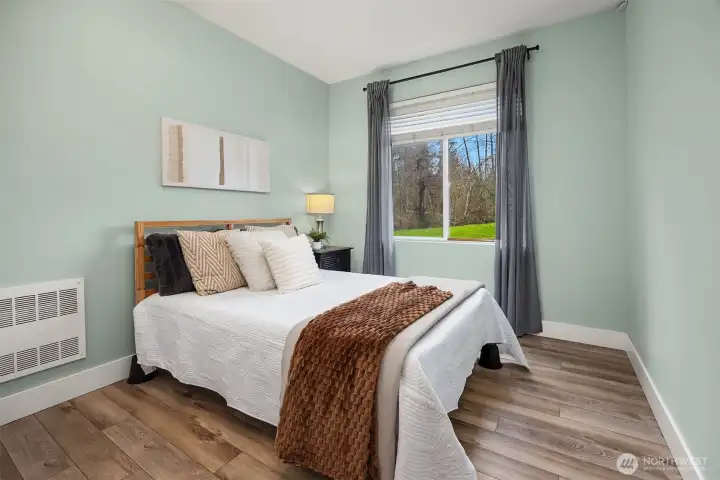Another well-sized bedroom features soft, neutral tones, warm flooring, and a bright window, a comfortable and inviting space that offers flexibility for guests, a home office, or personal retreat.