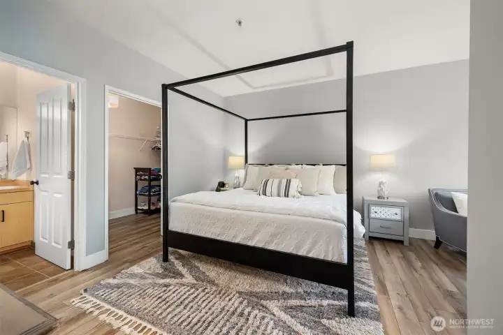 The elegant primary suite offers a spacious and serene retreat, featuring warm flooring, soft neutral tones, and a stylish four-poster bed, with the beautifully appointed en-suite bath conveniently accessible just beyond.