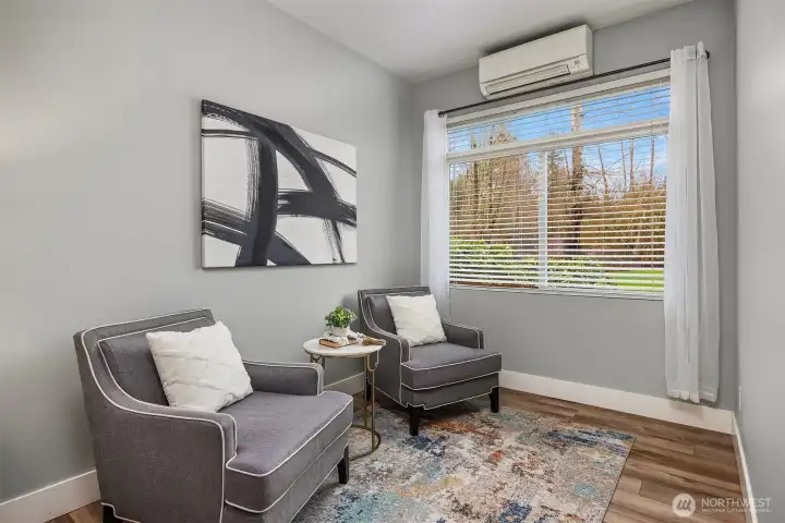 This cozy sitting area within the primary suite offers a quiet corner to unwind, with warm flooring, a bright window framing green views, and a relaxed, comfortable atmosphere perfect for reading or enjoying a moment of calm.