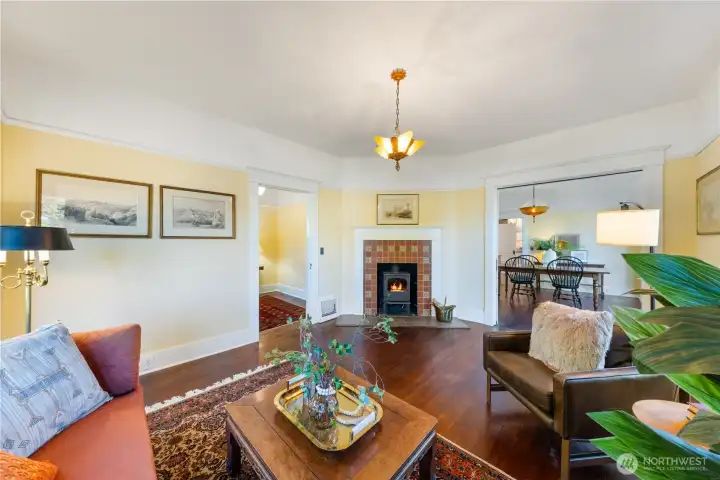 Beautiful Main living room space, wood burning fireplace, original fir flooring, and push button switches.  You can see the entry foyer to the left of the fireplace.  The formal dining room can be seen through the far doorway.