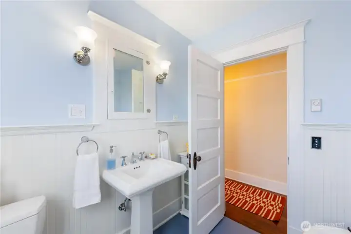 There are push-button switches and a storage cabinet behind the door.  You can see the hallway through the door.  To the left of the bathroom door at the end is the Bedroom.