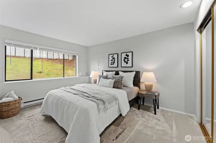Serene bedroom featuring plush carpet, soft neutral tones, and a large window that fills the room with natural light. Generously sized with space for a king bed, mirrored closet doors, and a peaceful outlook—an ideal retreat at the end of the day.