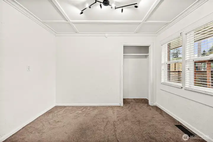 Main floor den/office or bedroom with large windows looking out to front yard featuring a built-in closet nook, wall to wall carpeting, track lighting piece, coffered ceiling adding an architectural design detail.