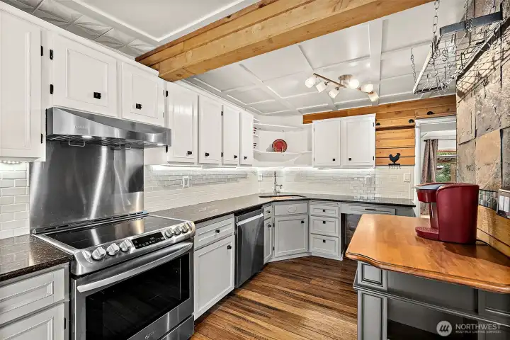 Stainless appliances with glass top stove and stainless backing and oven hood. White subway backsplash wraps around the kitchen. Exposed wooden beam ties in with the hardwood floors and modern farmhouse charm of the kitchen.