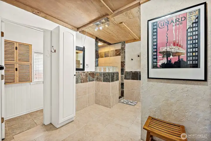 Large 3/4 bathroom features ceramic tile flooring and backsplash. Tiled walk-in shower area with overhead light. Wood paneled ceiling and track lighting fixturing.