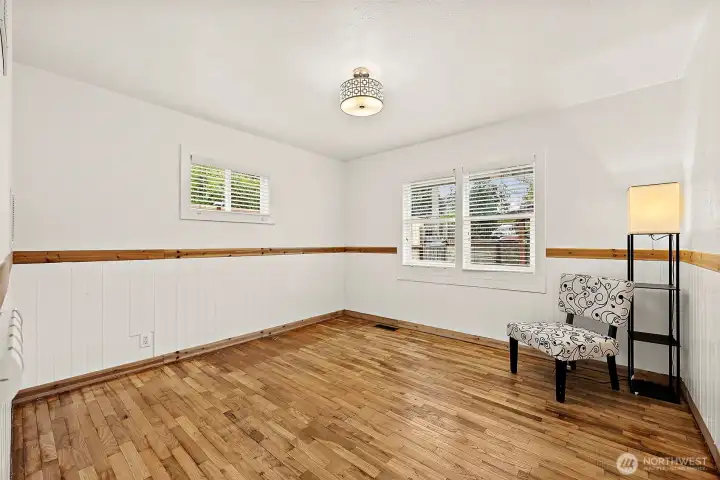 Main floor bedroom with hardwood floors with a wood chair rail designed walls. Flush mount modern lighting fixture and 2 windows to bring light into the room. This room faces the front yard.