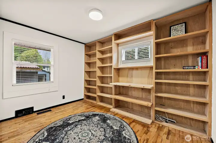 Office/den with a full wall of built-ins and hardwood floors. Large window looks out toward the detached garage/shop and small window looks out to side driveway.