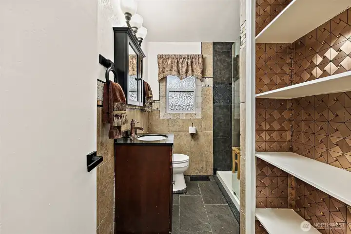 Second 3/4 bathroom located on the main floor, featuring, dark wood vanity with inset sink,  walk-in shower with tiled shower wall and glass panel, ceramic tile flooring.