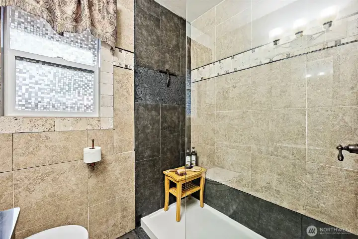 The walk-in shower with tiled shower wall and glass panel situated across from toilet and vanity in the bathroom.