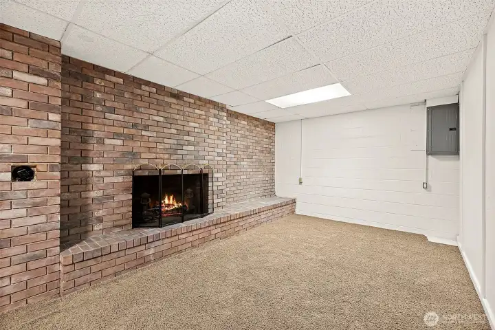 Floor to ceiling brick fireplace serves as focal point of basement bonus living room space, complete  with raised hearth for seating, storage or decorating options. You can also find the electrical panel in this room. Wall to wall carpeting, drop ceiling with integrated lighting