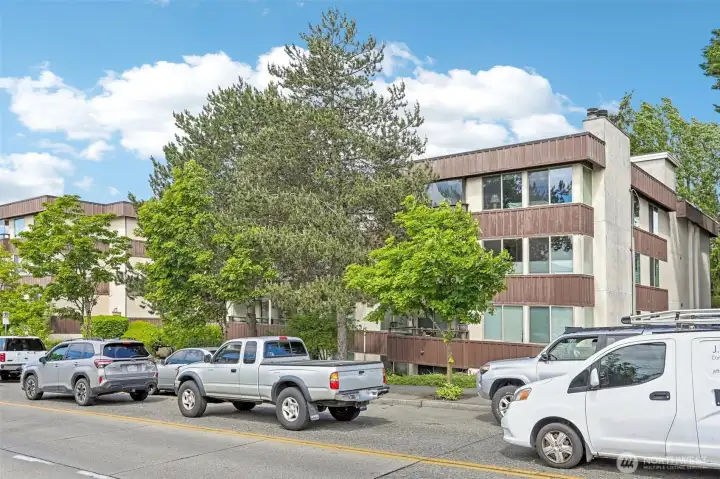 Well-maintained building exterior with lush trees, ample parking, and classic Pacific Northwest charm.