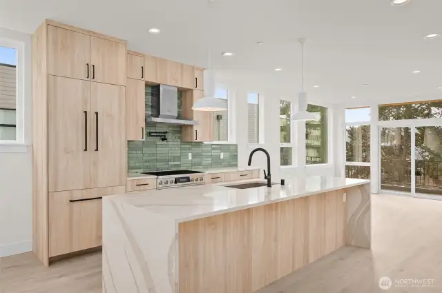 Boasting an elongated floating island, this bright kitchen features breakfast bar seating, flush refrigerator, and tasteful green backsplash.