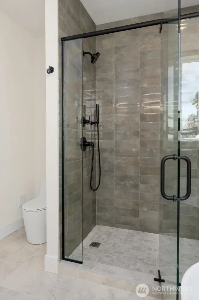 The primary shower features floor-to-ceiling custom tilework, and dual-nozzle hardware.