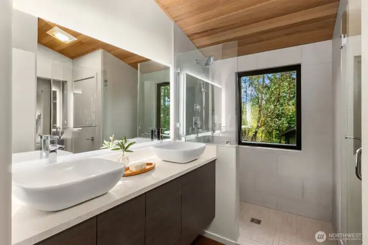 The bathroom, connected to both the hallway and primary suite. This sleek bathroom has modern fixtures and finishes, dual sinks and an oversized shower with a view of the garden. Pocket doors can close off the spaces for privacy.