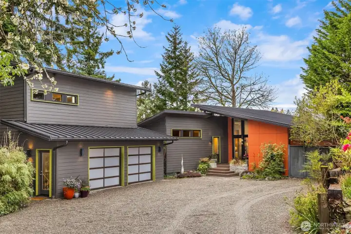 Another look at the front of the home and the 2-car garage with a studio and 3/4 bath above. The exterior features a standing seam metal roof, color-through Hardie Plank siding, and Cembrit cement fiber board panels, with metal-clad cedar trim and fascia. The home is also equipped with an auto-on Generac generator and a Level 2 EV charger in the garage.