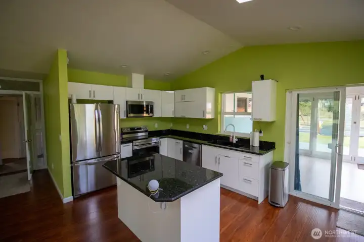 Bright kitchen with a granite center island, stainless refrigerator, dishwasher, and microwave, and ample cabinet storage. Bright kitchen with a granite center island, stainless refrigerator, dishwasher, and microwave, and ample cabinet storage.
