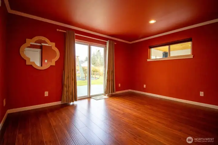 Spacious primary bedroom with rich hardwood floors, a French door to the deck, and an interior window to the adjoining sunroom Spacious primary bedroom with rich hardwood floors, a French door to the deck, and an interior window to the adjoining sunroom