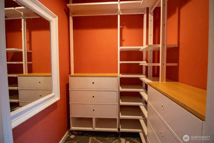 Custom-outfitted primary walk-in closet with built-in shelving, drawer banks, hanging rods, and a mirror. Custom-outfitted primary walk-in closet with built-in shelving, drawer banks, hanging rods, and a mirror.