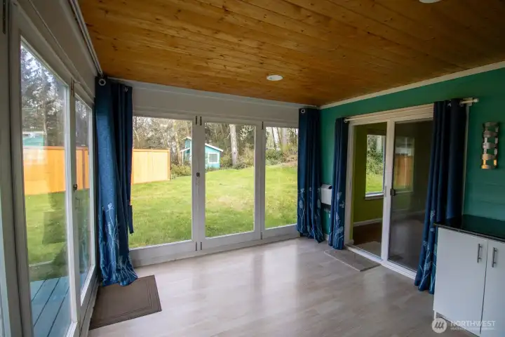 Window-wrapped sunroom with a wood-paneled ceiling, granite-topped storage, and backyard views. Window-wrapped sunroom with a wood-paneled ceiling, granite-topped storage, and backyard views.