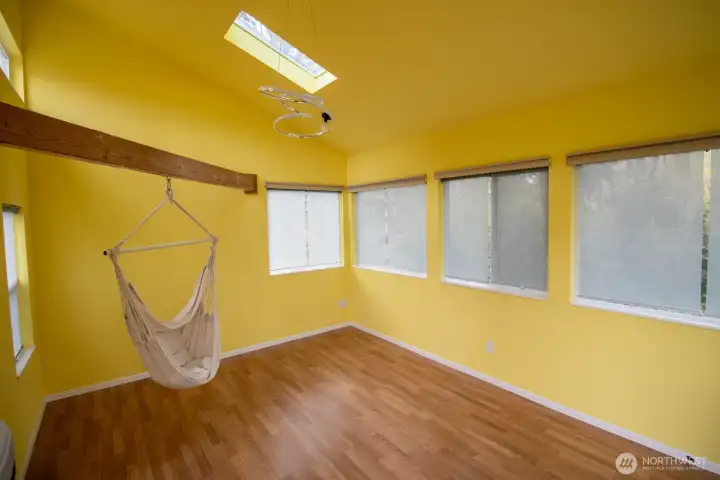 Cheerful studio interior featuring a skylight, exposed beam, and abundant windows with a fun swing chair. Cheerful studio interior featuring a skylight, exposed beam, and abundant windows with a fun swing chair.