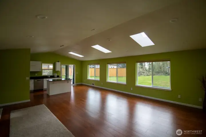 Spacious living area flowing into the kitchen, framed by a wall of windows and hardwood floors. Fully insulated ceiling. Spacious living area flowing into the kitchen, framed by a wall of windows and hardwood floors. Fully insulated ceiling.