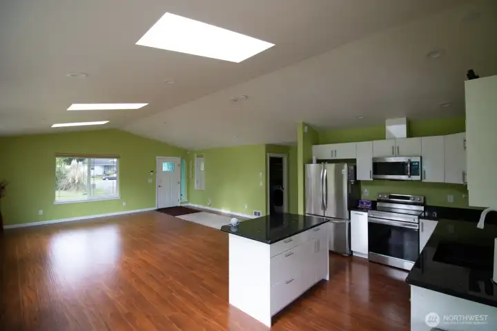 Open-concept living room and kitchen with a vaulted, skylit ceiling, granite island, and rich hardwood floor. Open-concept living room and kitchen with a vaulted, skylit ceiling, granite island, and rich hardwood floor.