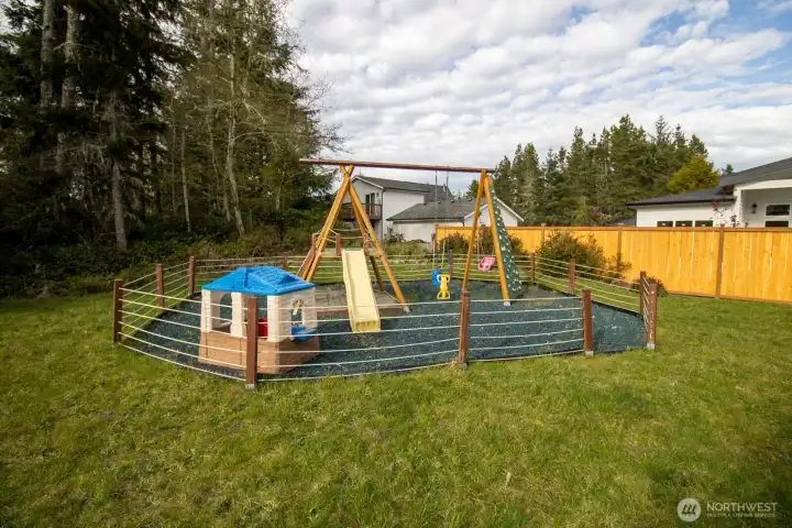 Custom-built playground with a swing set, slide, climbing wall, and sand pit, in a fenced yard. Custom-built playground with a swing set, slide, climbing wall, and sand pit, in a fenced yard.