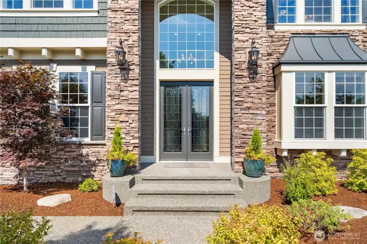 Grand double-door entry framed by stonework, planters, and elegant exterior lighting creates a warm, upscale welcome.