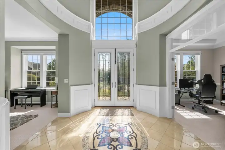 Sunlit entry with soaring windows and glass-paneled doors, opening to versatile office/den and living room.