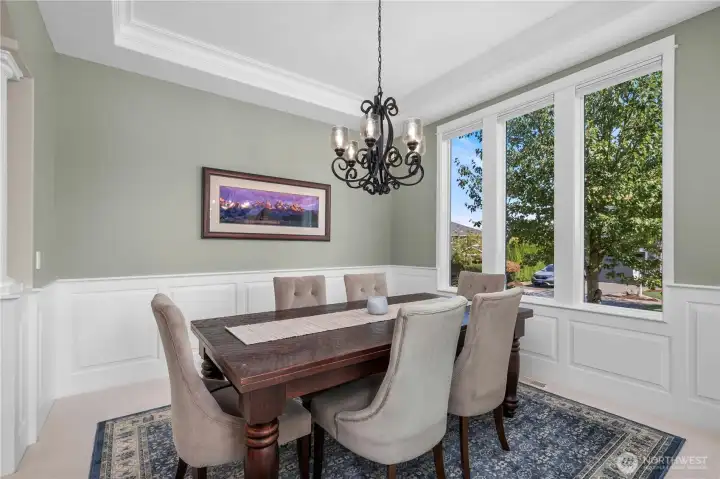 Formal dining room with wainscoting, large windows, and a stylish chandelier, perfect for entertaining.