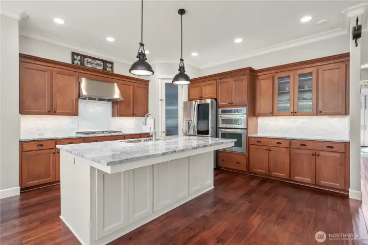 Chef’s kitchen with rich wood cabinetry, custom backsplash, stainless appliances, and expansive prep space.