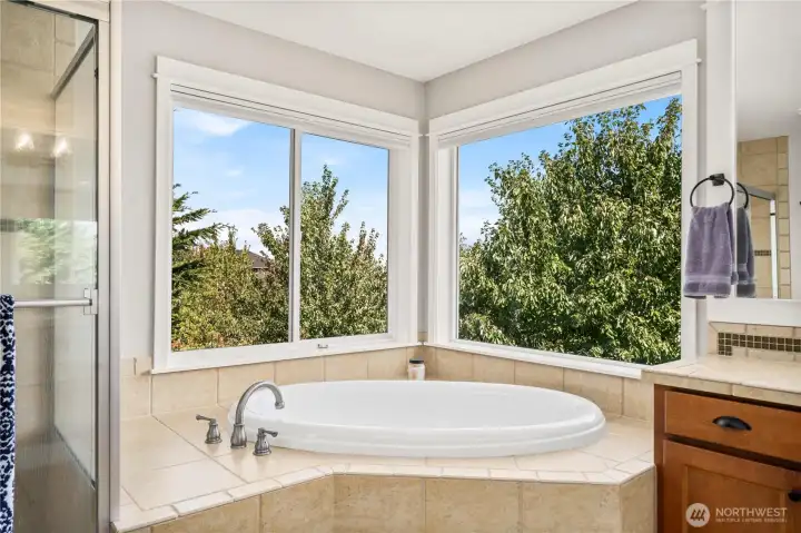 Corner soaking tub framed by large windows, offering a spa-like experience with peaceful treetop views.