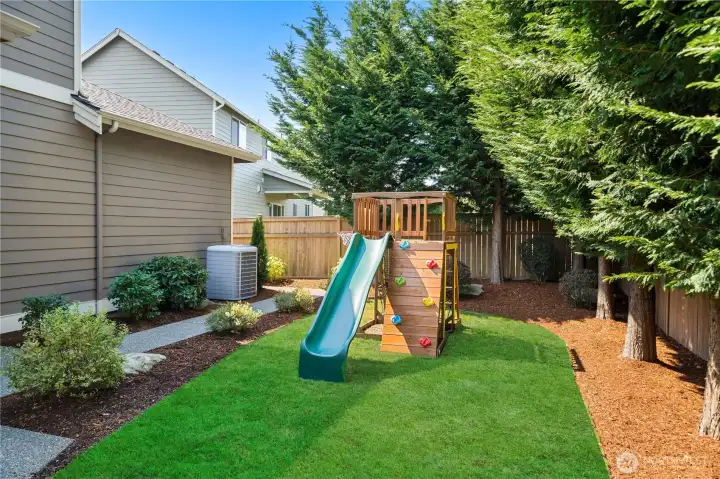 Fully fenced yard with mature landscaping and playset, perfect for gatherings or everyday fun.
