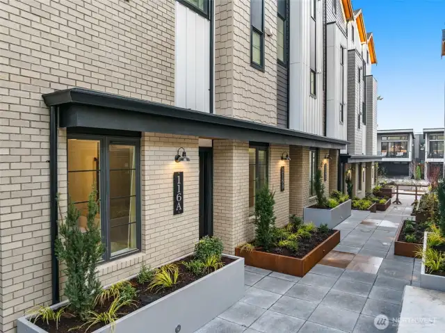 Each entry is uniquely framed by curated greenery, bold black accents, and timeless brick—urban design meets private comfort at every doorstep.